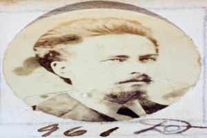 Ein altes Foto eines Mannes mit Schnurrbart und Bart, der direkt in die Kamera schaut und einen ernsten und nachdenklichen Ausdruck hat.