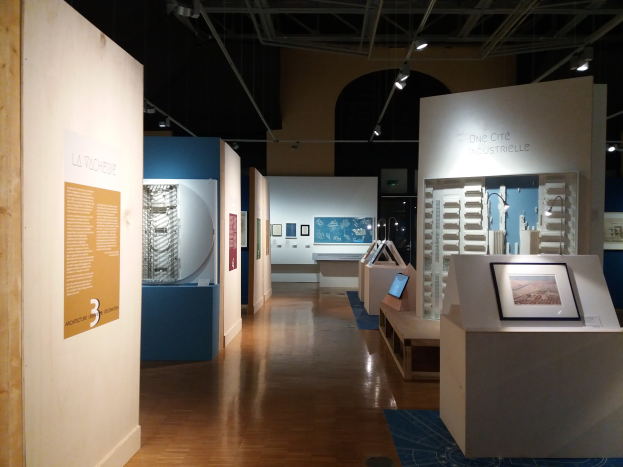 Ein Raum voller verschiedener Kunstwerke, darunter Fotorahmen auf Tischen, Texttafeln an den Wänden, Deckenleuchten und ein Teppichboden im Museum of Modern Art.