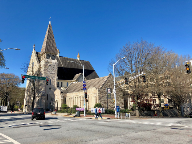 St. Luke's Episcopal Church, eine große Kirche mit einem Turm, steht an einer Straßenecke umgeben von Gebäuden, Verkehr, Fußgängern und Grün unter einem klaren blauen Himmel.