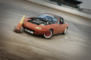 Eine Person fährt ein rotes Auto mit hoher Geschwindigkeit auf einer Rennstrecke, mit einem Verkehrskegel vor ihnen.