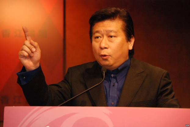 Ein Mann im Anzug und Krawatte, der eine Rede an einem Rednerpult mit einem Mikrofon hält und ernst dreinschaut.