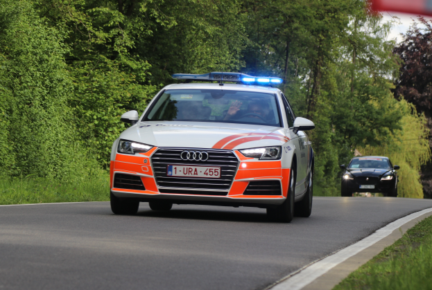 Ein Audi A4 Polizeiwagen fährt auf einer Straße neben einem Wald, mit zwei Personen darin, gesäumt von Gras auf beiden Seiten und einem klaren blauen Himmel im Hintergrund.