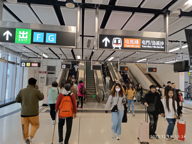 Menschen mit Gepäck durch einen geschlossenen Flughafen, Rolltreppen, Informationsanzeigen, Deckenleuchten und Glaswände im Hintergrund.