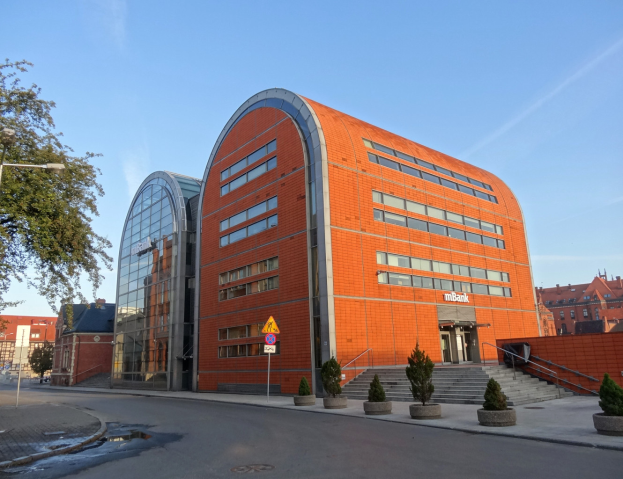 Ein großes oranges IBM-Hauptquartier-Gebäude mit zahlreichen Fenstern, umgeben von Straßeninfrastruktur, Fahrzeugen und Topfpflanzen unter einem bewölkten Himmel.