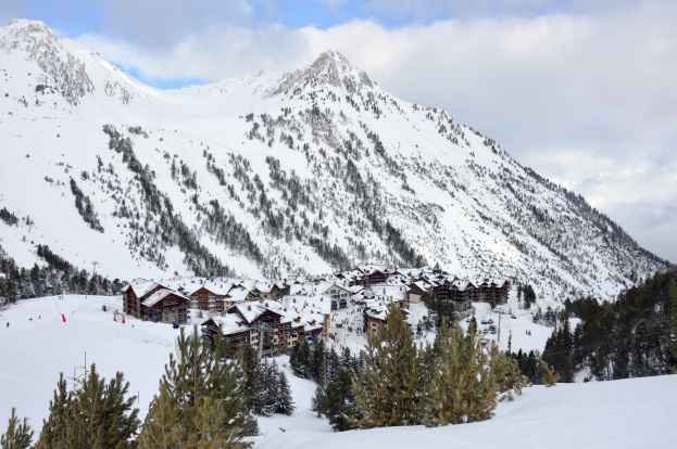 Ein Skigebiet mit schneebedeckten Bergen im Hintergrund, eine Skihütte zwischen schneebedeckten Bäumen und ein bewölkter Himmel.