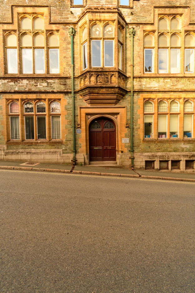 Altes Gebäude mit vielen Fenstern und einer hölzernen Tür, das an einer Straße liegt und Rohre an seinen Wänden hat.