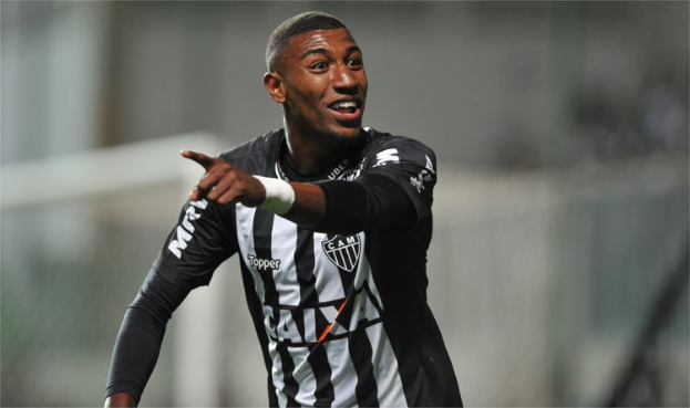 Fußballspieler in einem schwarz-weißen gestreiftem Trikot, der grinsend nach einem Tor jubelt, Hintergrund unscharf.