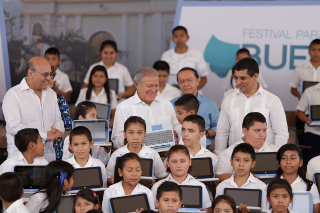 Eine Gruppe von Kindern sitzt vor einer Menge von Menschen mit Laptops, im Hintergrund eine Wand mit der Aufschrift "Festival Paraiso Blue".