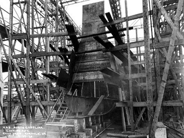 Schwarzes und weißes Foto eines Schiffs in einem Schiffbau, mit hölzernen Pfählen und Treppen im Vordergrund und Himmel im Hintergrund, mit Text "Marine-Waffensysteme" links unten.