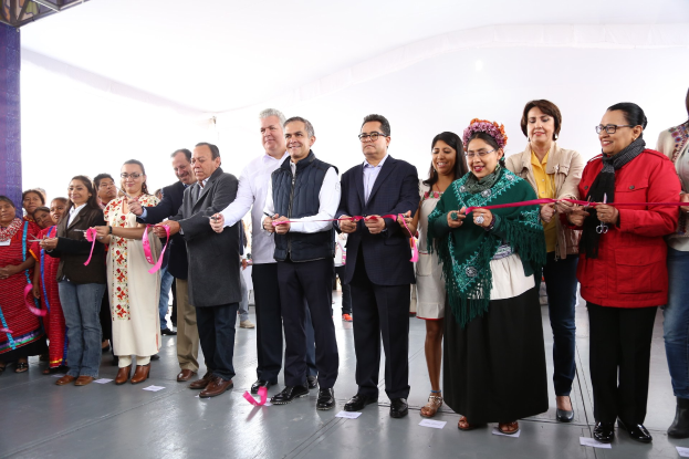 Eine Gruppe von Menschen, die eine Schnur durchschneiden, mit einer Säule links, verstreuten Papieren auf dem Boden und einem weißen Tuch im Hintergrund.