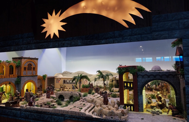 Eine Krippe-Ausstellung im Museum mit Figuren, Tieren, Gebäuden und Pflanzen, beleuchtet von oben an der Wand.