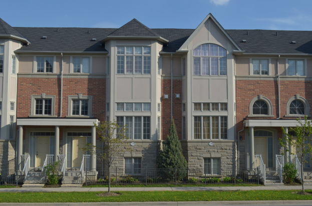 Eine Reihe von Stadthäusern in einem Wohnviertel mit Fenstern, Türen, Säulen, Geländern, Treppen, Pflanzen, Bäumen, Gras und Himmel.