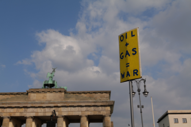 Das Brandenburgertor in Berlin, Deutschland, mit einem gelben Schild, auf dem "Öl- und Gaskrieg" steht, im Vordergrund, Gebäuden, Polen, Lichtern, einer Statue und einem bewölkten Himmel im Hintergrund.
