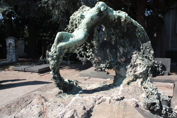 Ein Friedhof mit zahlreichen Gräbern umgeben von vielen Bäumen, mit einer Skulptur im Vordergrund.