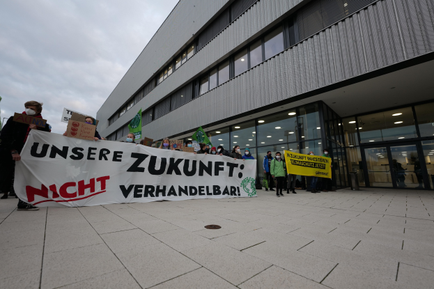 Menschen halten ein Banner mit der Aufschrift "Unsere Zukunft Verhandelbar" ("Wir haben keine Angst zu kämpfen") vor einem Glasgebäude bei Nacht.