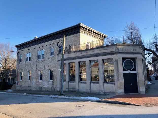 Altes zweistöckiges Backsteingebäude mit der Aufschrift "College Hill Bibliothek" an einer Straßenecke mit Bäumen, Strommasten, Drähten, geparkten Autos und einem sichtbaren Himmel.