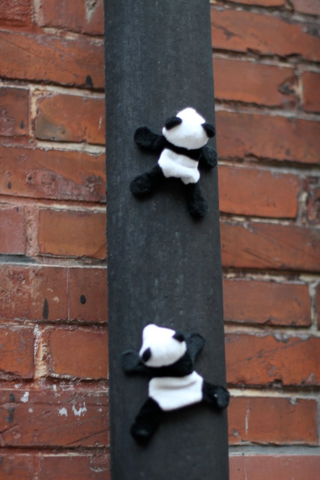 Panda-Spielzeuge an einem Holzstab vor einer Backsteinwand.