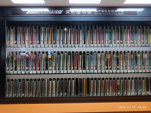 Eine gut beleuchtete Bibliothek mit zahlreichen Büchern auf Regalen, ein Textschild und ein Wasserzeichen unten, das wie eine Selbstbedienungsbibliothek von Stadtvierteln aussieht.