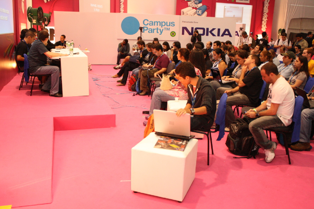Eine Konferenz mit Sitzenden, die den Rednern auf der Bühne lauschen, mit einem großen Banner und einer Wand im Hintergrund.