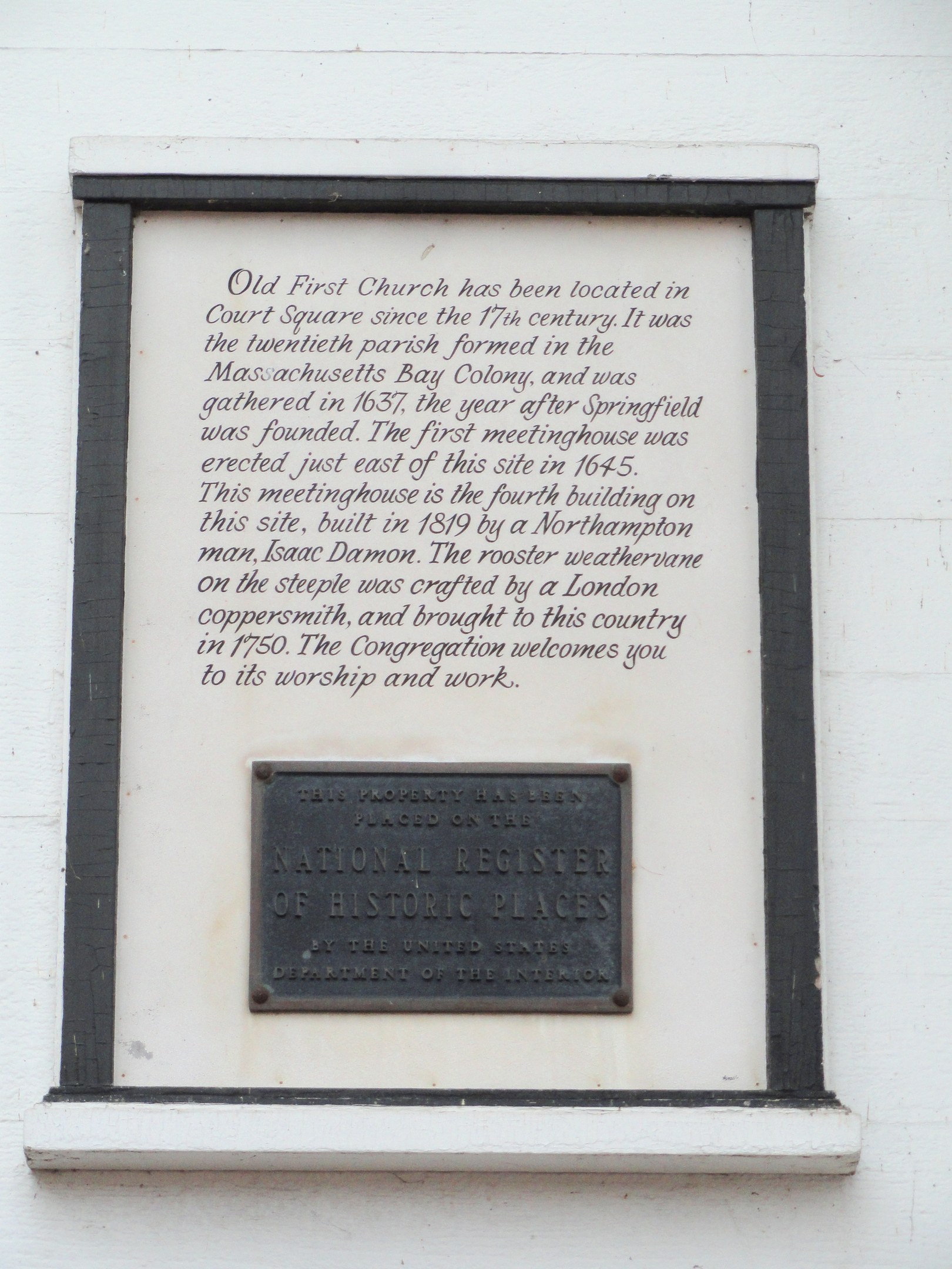Plaque auf einer Gebäudewand mit der Aufschrift "National Register of Historic Places" in fetter Schrift, umgeben von einem dekorativen Rahmen, auf dunklem Material montiert.