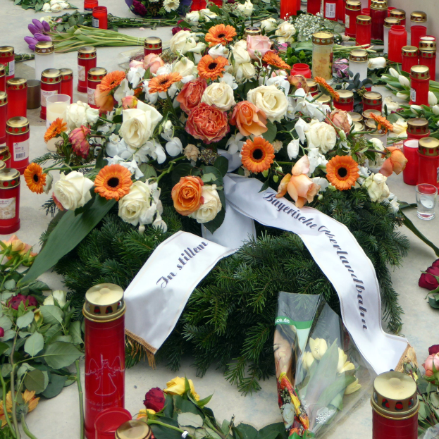 Mahnmal in Berlin, Deutschland, mit Blumen und Kerzen, die vor einer Wand auf dem Boden plaziert sind.