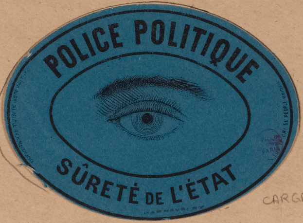 Ein brauner Karton mit einem blauen Aufkleber, auf dem "Police Politique Süreté de L'√Čtat" und ein Auge in der Mitte steht.
