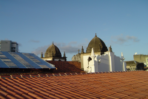 Stadtlandschaft mit Gebäuden im Vordergrund, Solarpanels auf einem Dach und einem blauen Himmel im Hintergrund.