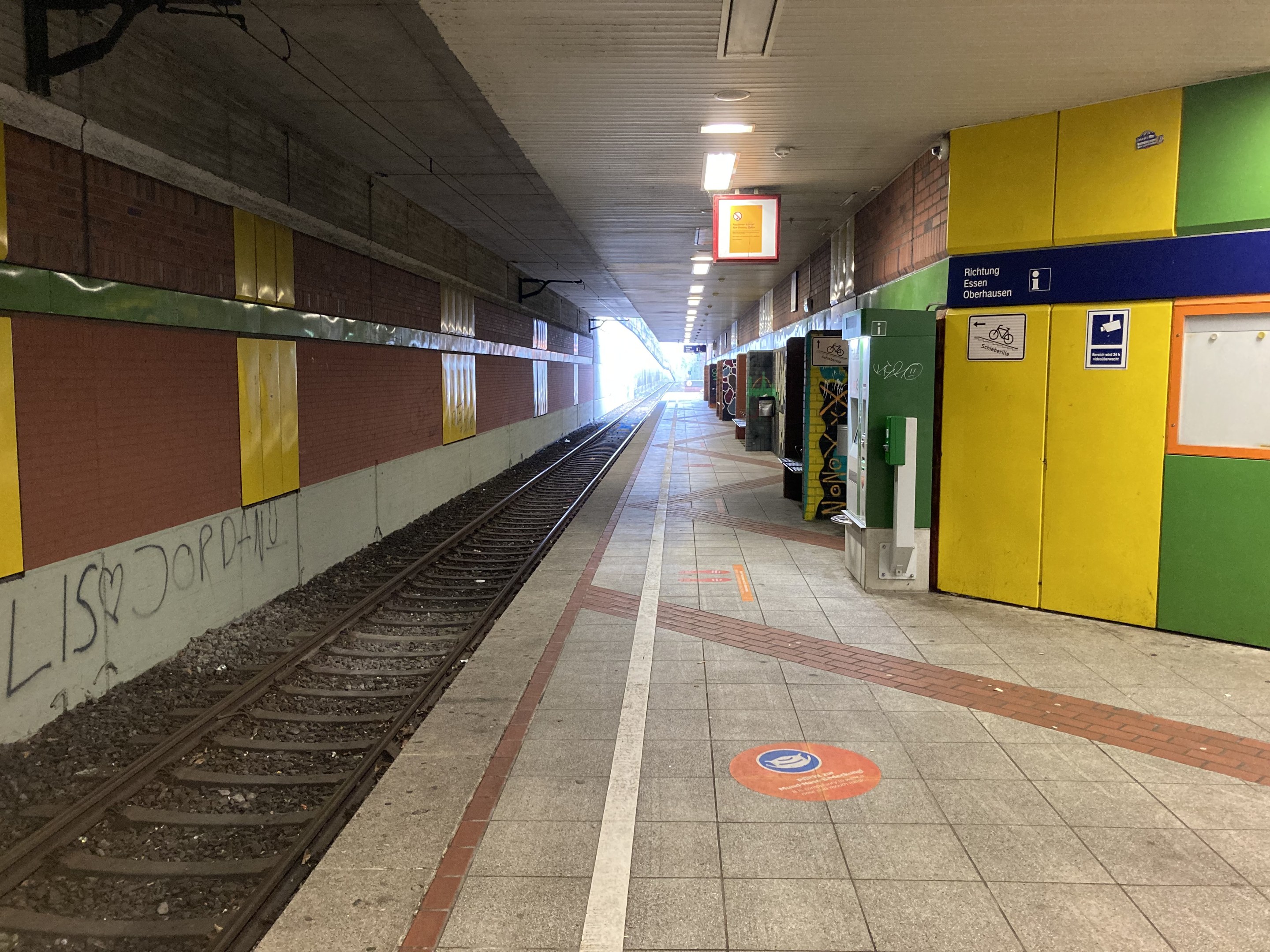 Ein Bahnsteig mit einem Zug auf den Schienen, beleuchtet von Deckenlampen, mit Graffiti an einer linken Wand und ein paar Gegenständen auf der rechten Seite, identifiziert als Berlin Hauptbahnhof in Berlin, Deutschland.