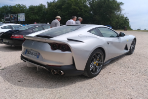 Roter Ferrari 812 Superfast auf dem Goodwood Festival of Speed, umgeben von Menschen mit Mützen, Bäumen, Texttafeln und einem bewölkten Himmel.